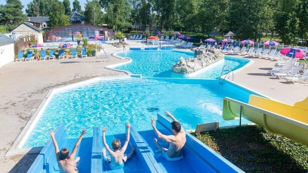 A swimming pool with a water slide, lounge chairs, and umbrellas.