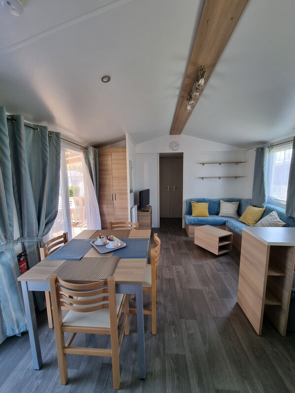 A modern, well-lit room with a dining table, chairs, a sofa, and a TV.