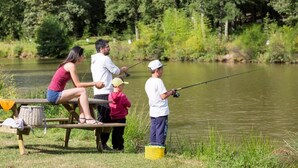 A family by a calm lake with a picnic table and a fishing rod.
