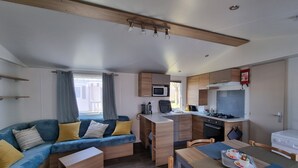 A compact living space with a sofa, a dining table, a kitchenette, and a window with curtains.