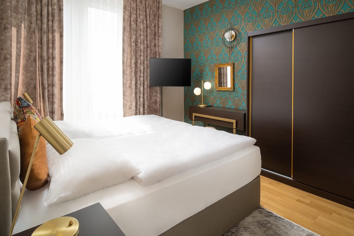 Moderni hotellihuone, jossa on siististi pedattu sänky, yöpöytä lampun kanssa, televisio ja vaatekaappi.