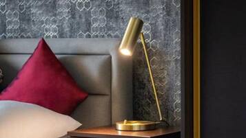 A neatly made bed with a red pillow, a bedside table with a lamp, and a patterned wallpaper.
