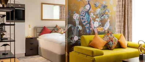 Una habitación de hotel moderna con una cama, un sofá amarillo, un cuadro de pájaros y flores, un escritorio con lámpara y un espejo.