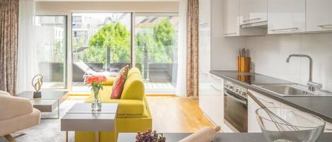 A modern living room with a yellow sofa, a coffee table with grapes and eggs, and a kitchen with a sink and utensils.