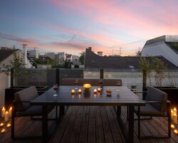 Una terrazza sul tetto con un tavolo apparecchiato per due, circondata da candele e bicchieri di vino, con vista su un panorama urbano al tramonto.
