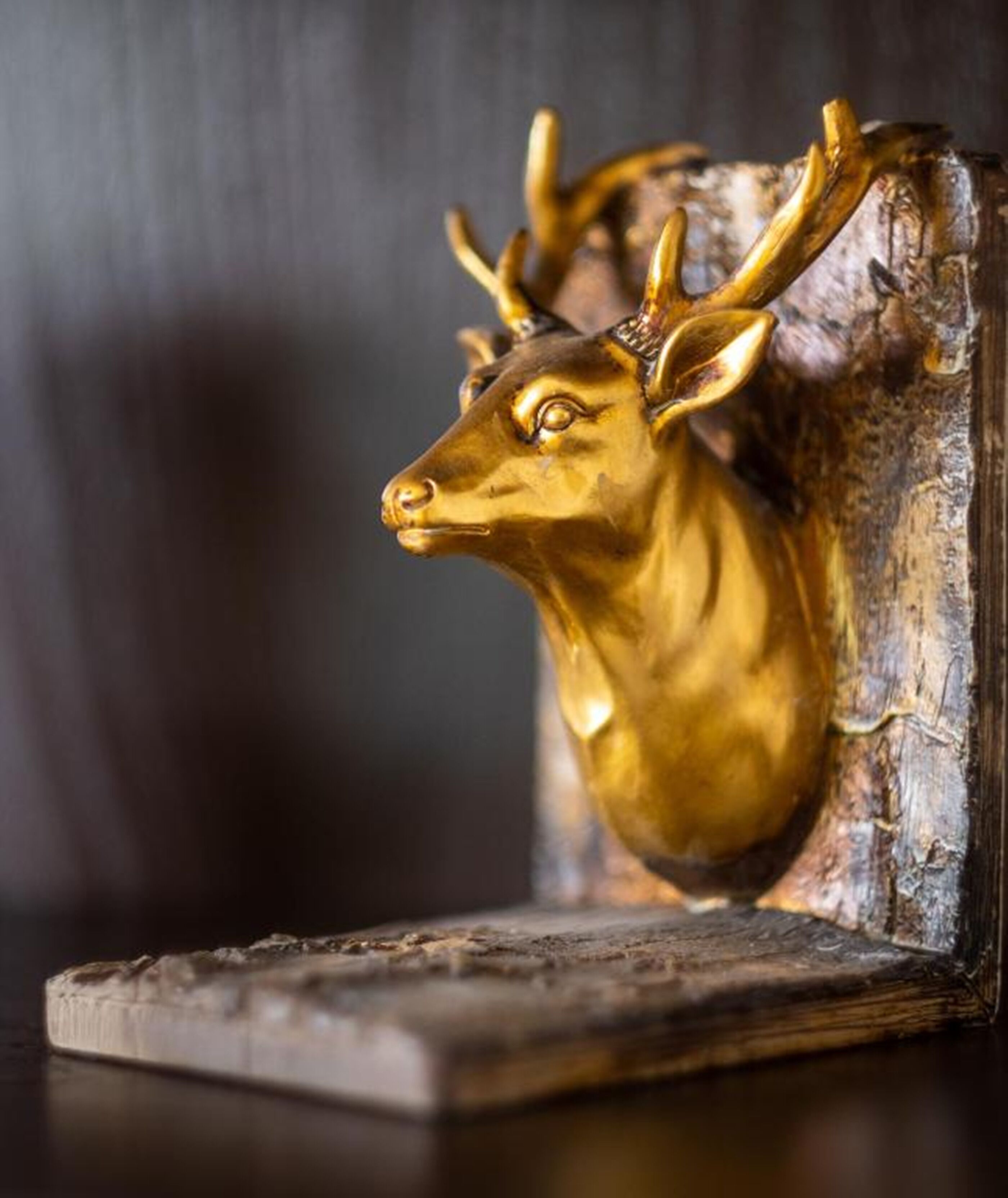 Een gouden beeldhouwwerk van een hertenhoofd op een ruwe houten voet.
