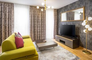 A modern living room with a yellow sofa, a flat-screen TV, a coffee table, and a large mirror with lights. - Abieshomes Serviced Apartments - Schönbrunn (Vienna)