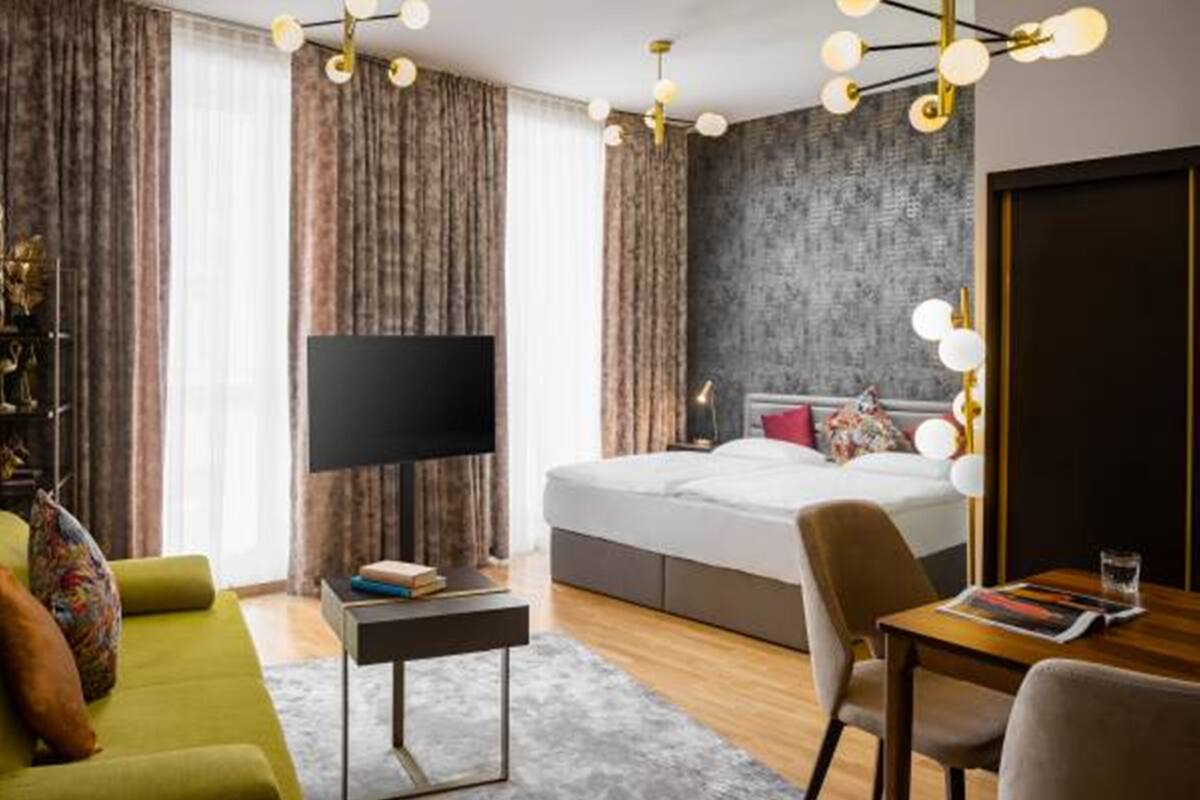 Moderni hotellihuone, jossa on suuri sänky, taulutelevisio, työpöytä tuolilla ja ruokapöytä.
