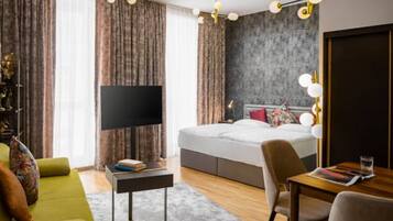A modern hotel room with a large bed, a flat-screen TV, a desk with a chair, and a dining table.