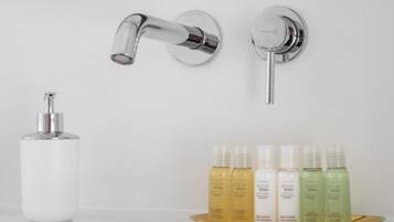 Un baño con un grifo moderno, un dispensador de jabón y una bandeja con cinco botellas de productos de cuidado corporal Aqua Series.