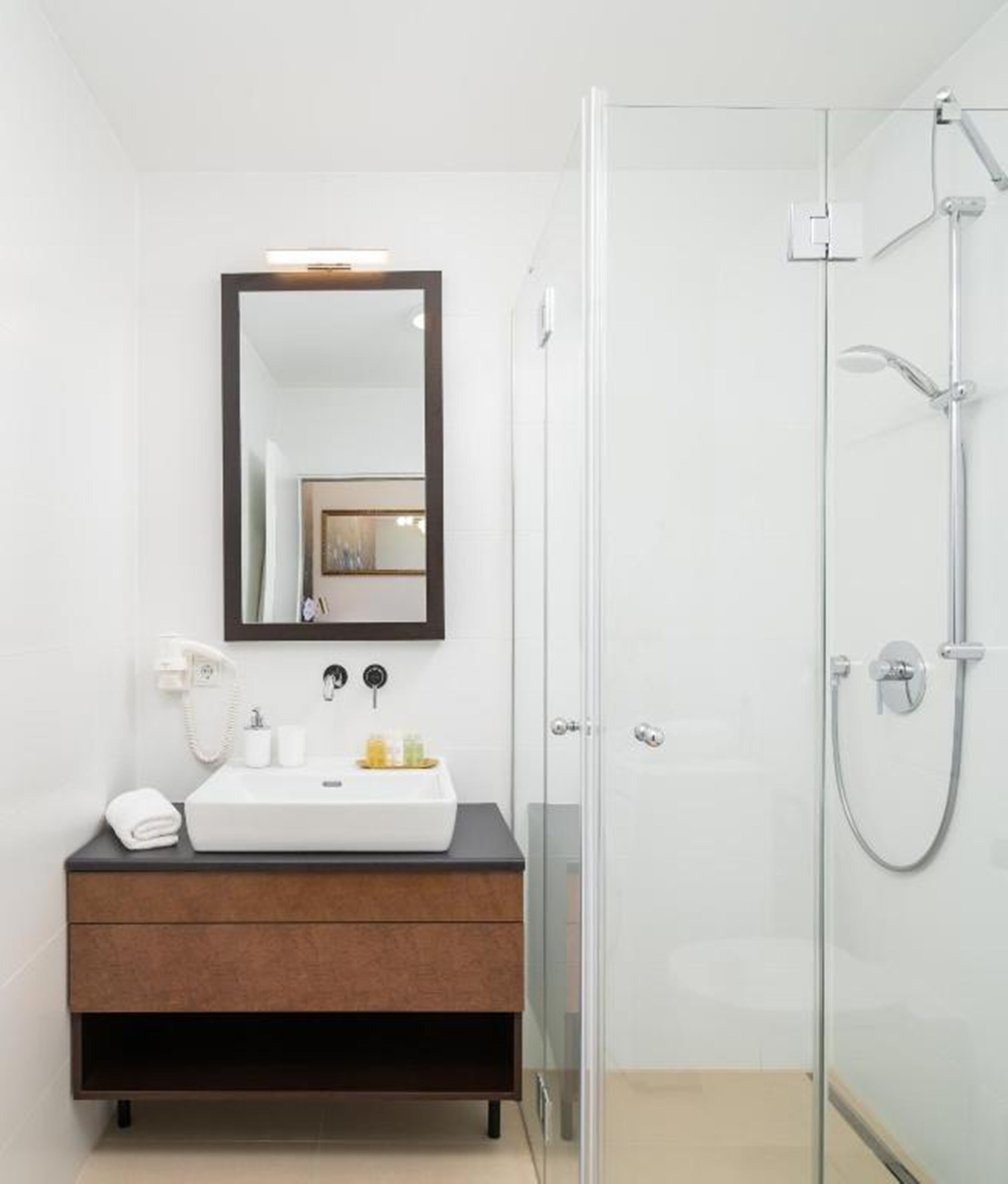 A modern bathroom with a glass shower enclosure, a white sink with a dark countertop, and a large mirror above the sink.