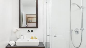 A modern bathroom with a glass shower enclosure, a white sink with a dark countertop, and a large mirror above the sink.