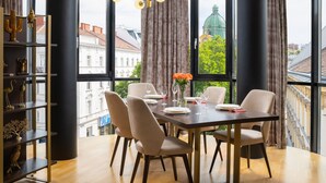 Un comedor con una mesa dispuesta para cuatro, ventanas amplias y vistas a edificios y zonas verdes.
