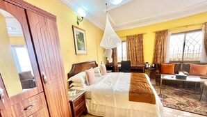 A spacious bedroom with a large bed, a wooden wardrobe, a sitting area with a sofa and armchairs, and a dining table. - Seaside Suites and Hotel Room #101 (Freetown)