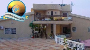 A two-story building with a balcony, a terrace, and a pool area. - Seaside Suites and Hotel Room #101 (Freetown)
