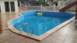 An indoor swimming pool with a stone-tiled deck, a white railing, and a staircase leading to an upper level. - Seaside Suites and Hotel Room #101 (Freetown)