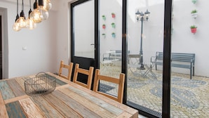 Ein Essbereich mit Holztisch und -stühlen, einer hängenden Leuchte und Blick auf den Innenhof durch Glastüren.