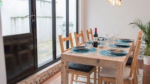 Un coin repas avec une table en bois dressée pour quatre personnes, une bouteille de vin rouge et une plante en pot.