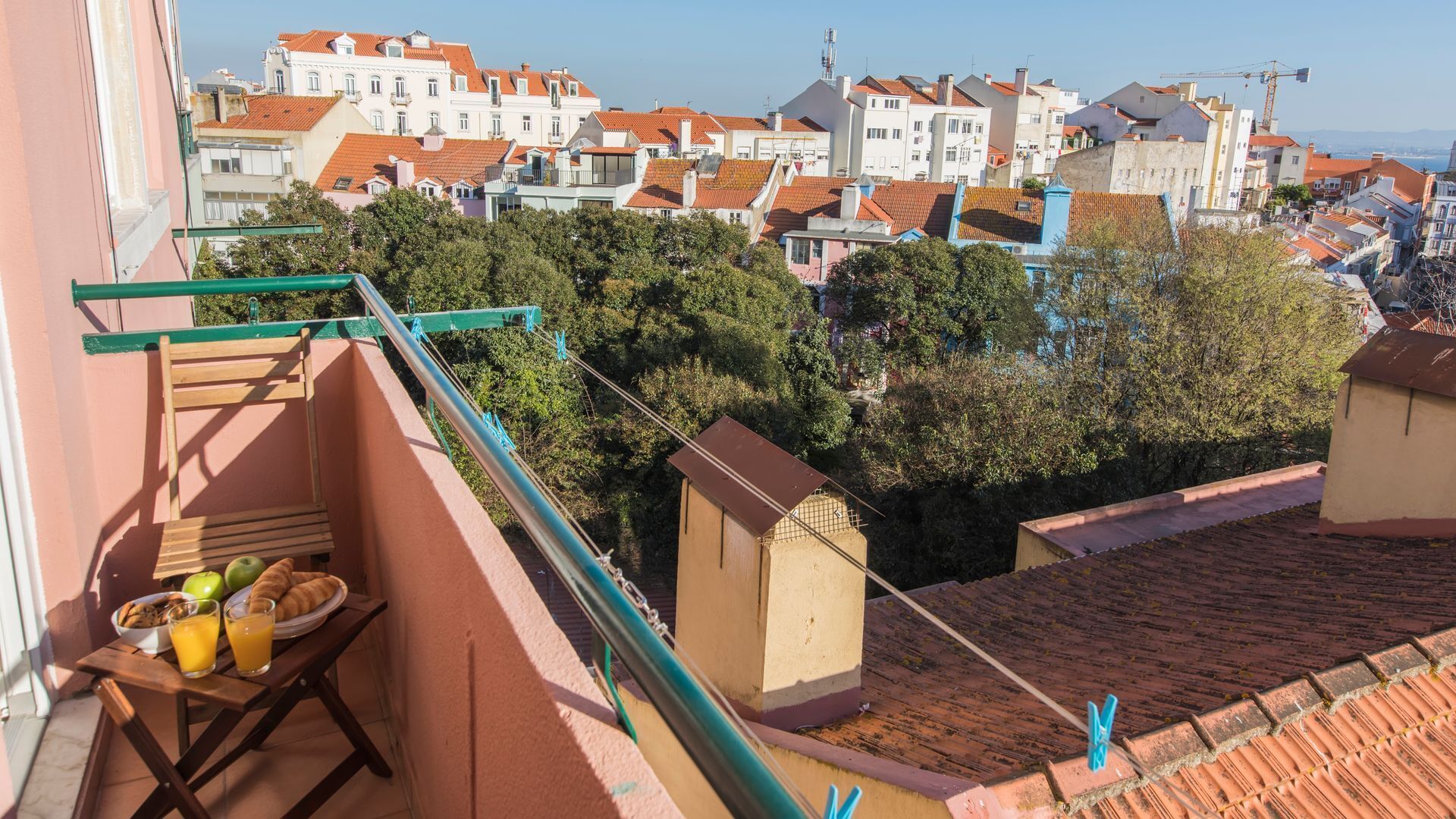 Un balcon avec une table dressée pour le petit-déjeuner, donnant sur un quartier résidentiel aux toits de tuiles rouges et à la végétation luxuriante.