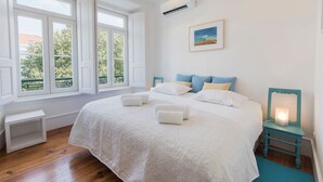 Ein Schlafzimmer mit einem großen Bett, einem Nachttisch mit Lampe, einem Fenster mit Blick auf Grünflächen und einem Gemälde an der Wand.