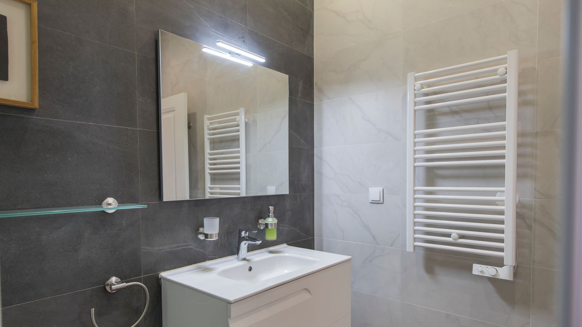 Een moderne badkamer met een witte wastafel, een spiegel, een handdoekrek en een douchehoek.