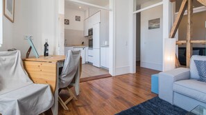 A modern living room with a wooden dining table, a sofa, and a kitchen in the background.