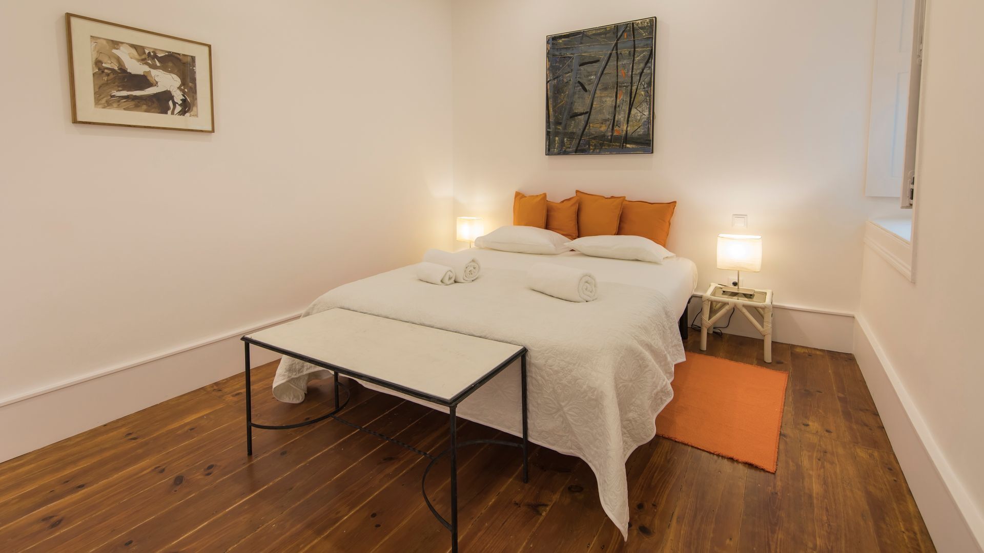 A bedroom with a bed, bedside tables, a nightstand, a table, and a painting on the wall.