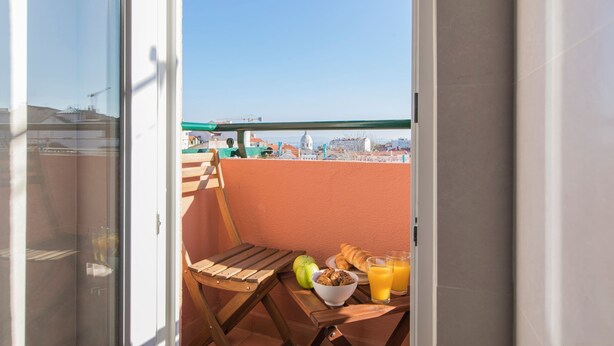 Ein Balkon mit einem Holzstuhl, einer Schüssel Kekse, einem Apfel und Gläsern Orangensaft.