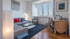Ein modernes Wohnzimmer mit einem grauen Sofa, einem Glastisch und einem Holznachttisch mit einer Flasche.