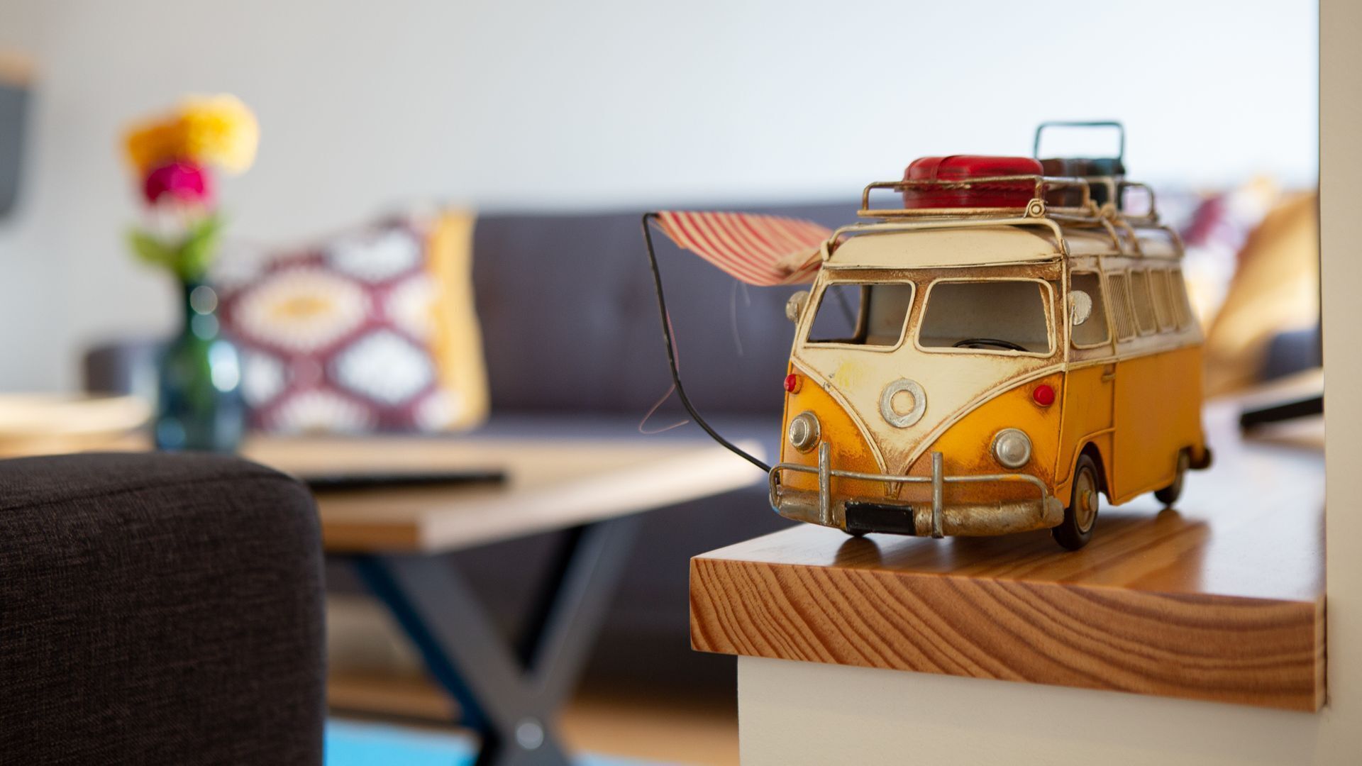 A toy van on a wooden shelf in a room with a couch and a table.