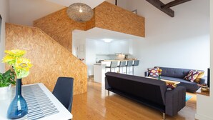 A modern living room with a wooden staircase, a dining area with a piano, and a kitchen in the background. - Oren Duke's House by LovelyStay (Porto)