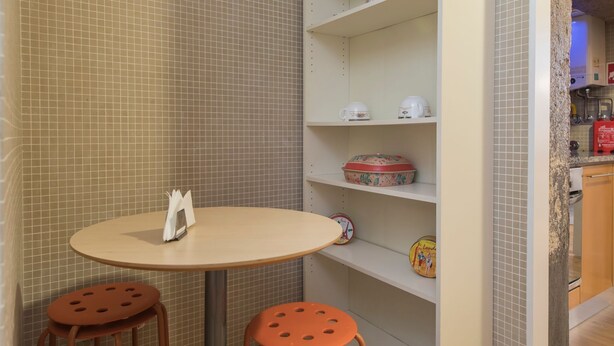 A small, tiled room with a round table, two stools, and shelves with decorative items. - Downtown Cosy Wonder by LovelyStay (Lisboa)
