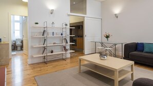 A modern living room with a wooden floor, a glass coffee table, a grey sofa, and a bookshelf. - Downtown Cosy Wonder by LovelyStay (Lisboa)