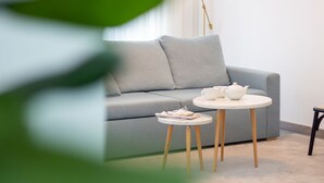 A modern living room with a grey sofa, a small round table with a white teapot and cups, and a book on the table.
