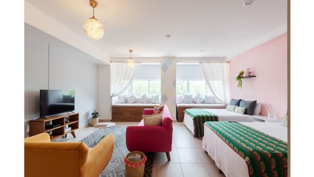 Una sala moderna con televisor, sofá, sillón y cama con colcha estampada.