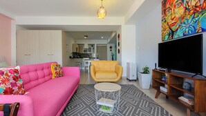 Una sala de estar moderna con un sofá rosa, un sillón amarillo y un mueble de TV con televisor de pantalla plana.