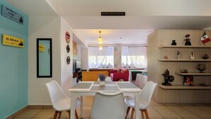 Un comedor con una mesa y sillas, una lámpara colgante, y vista al salón.