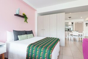 Une chambre moderne avec un lit, un bureau et un coin cuisine en arrière-plan.