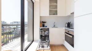 A modern kitchen with a dishwasher, sink, and stove, and a large window overlooking a cityscape. - Trindade Cozy Apartment by LovelyStay (Porto)