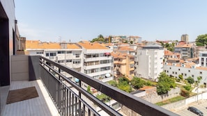 Ein Balkon mit Blick auf eine Stadtlandschaft, darunter Gebäude mit roten Ziegeldächern und eine Mischung aus moderner und traditioneller Architektur.