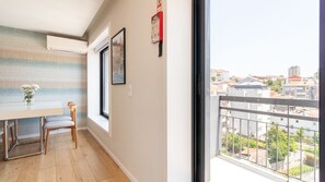 A room with a window, a table, two chairs, a vase with flowers, and a framed picture on the wall. - Trindade Cozy Apartment by LovelyStay (Porto)