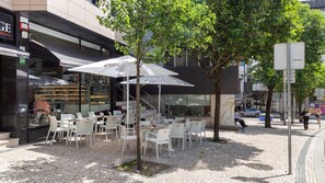 An outdoor café with white chairs and umbrellas, a staircase leading to an upper level, and a storefront with a glass display. - Trindade Cozy Apartment by LovelyStay (Porto)