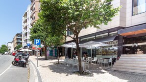 Eine Straße mit Baumreihen, Sitzgelegenheiten im Freien und einem Gebäude mit Schaufenster.