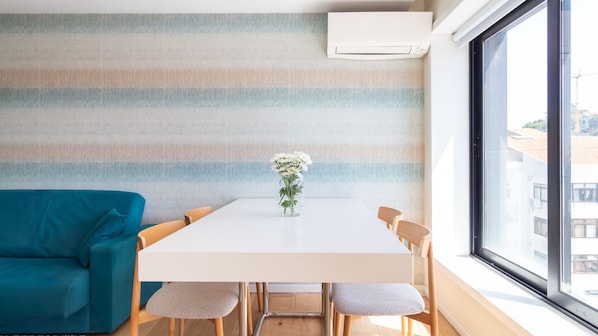 Ein modernes Zimmer mit einer gestreiften Wand, einem weißen Tisch mit Stühlen, einem blauen Sofa und einem Fenster mit Blick auf Gebäude.