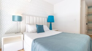 Ein Schlafzimmer mit einem weißen Bett, zwei Nachttischen und einer blauen Lampe auf jeder Seite, sowie einer Wand mit Muster.