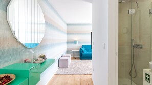 A modern bathroom with a glass shower enclosure, a white sink, and a blue sofa in the adjacent living area. - Trindade Cozy Apartment by LovelyStay (Porto)