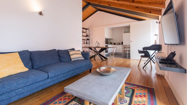 A living room with a blue sofa, a coffee table, and a rug. There is a kitchen in the background with a dining area.