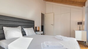 A bedroom with a large bed, a bedside table, a nightstand, a wardrobe, and a lamp.