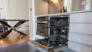 A modern kitchen with a built-in dishwasher, oven, and a dining area with a table and chairs.