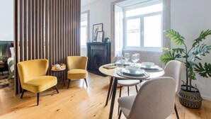 A modern dining area with a round table set for four, featuring a fireplace and large windows in the background. - Mouzinho Studio w/ AC in City Center by LovelyStay (Porto)